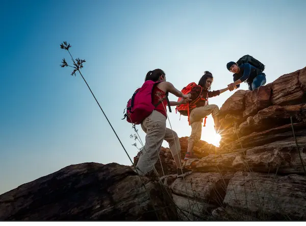 Group of hikers assisting each other during a trekking expedition on a rocky mountain.